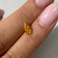 Vivid orange-yellow pear-shaped diamond with a brilliant cut, showcased on a soft, light background.