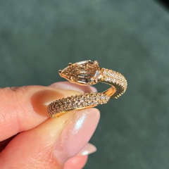 Gold snake-shaped bracelet with diamond accents held by a hand against a blurred green background