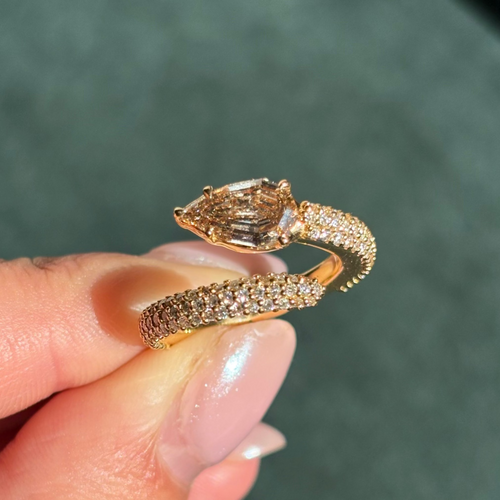 Gold snake-shaped bracelet with diamond accents held by a hand against a blurred green background