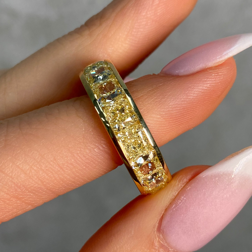 Gold ring with natural yellow diamonds on a finger against a neutral background