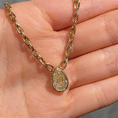 Gold necklace with a teardrop-shaped pendant held in a hand against a gray background