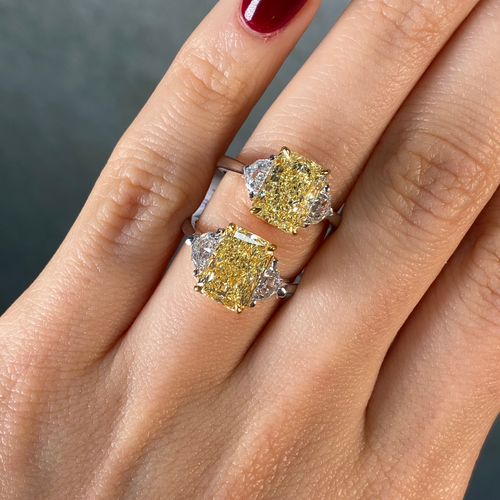 Two elongated radiant cut yellow diamond rings on a hand with a dark background