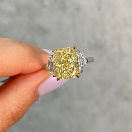fancy yellow diamond ring held by a hand against a gray background