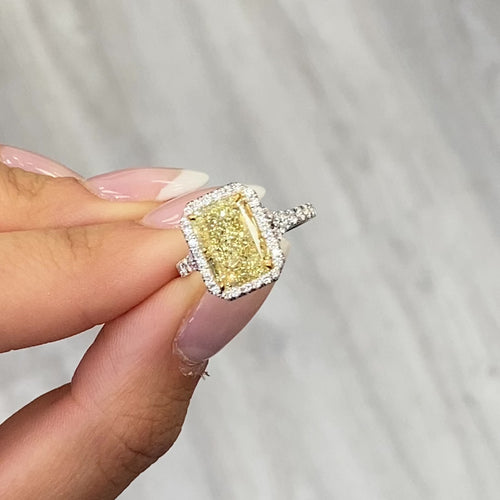 GIA certified light yellow elongated radiant diamond halo engagement ring with white diamonds.