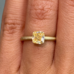 Vivid yellow-orange cushion-cut diamond with intricate facets, reflecting light on a soft background.