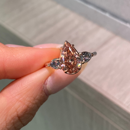 Unique three-stone ring with a deep brown-pink pear diamond and blue diamond accents, GIA certified.