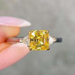 Vivid yellow diamond ring held by a hand against a neutral background