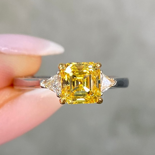 Vivid yellow diamond ring held by a hand against a neutral background