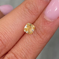 Vivid yellow-orange cushion-cut diamond with intricate facets, reflecting light on a soft background.