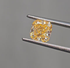 Vivid yellow-orange cushion-cut diamond with intricate facets, reflecting light on a soft background.